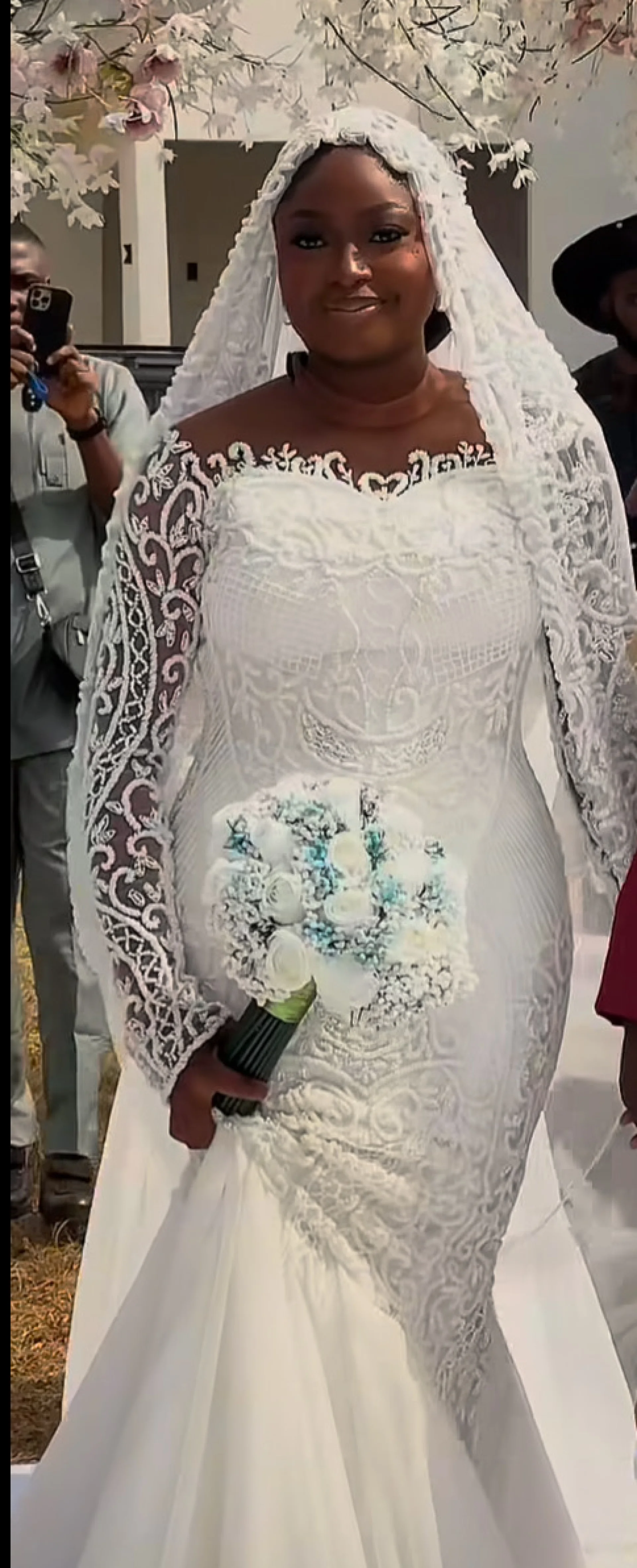 Bride in a long-sleeve lace gown and cathedral veil at an outdoor wedding