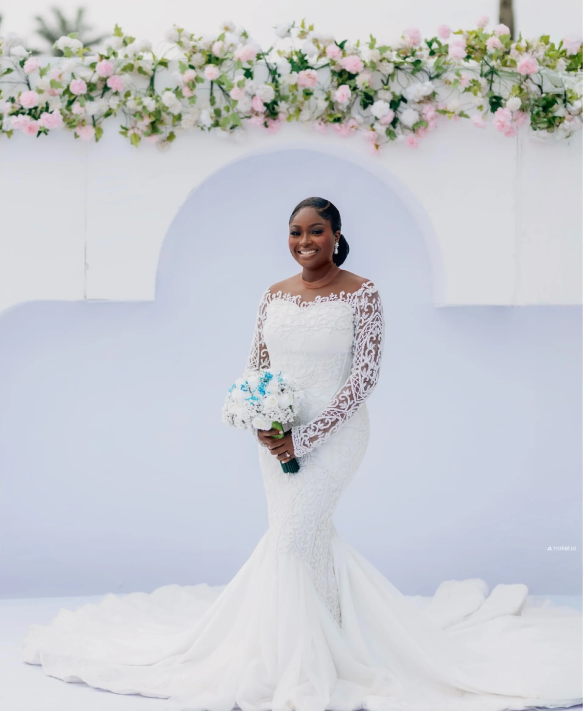 Bride smiling under a floral arch in a lace mermaid gown
