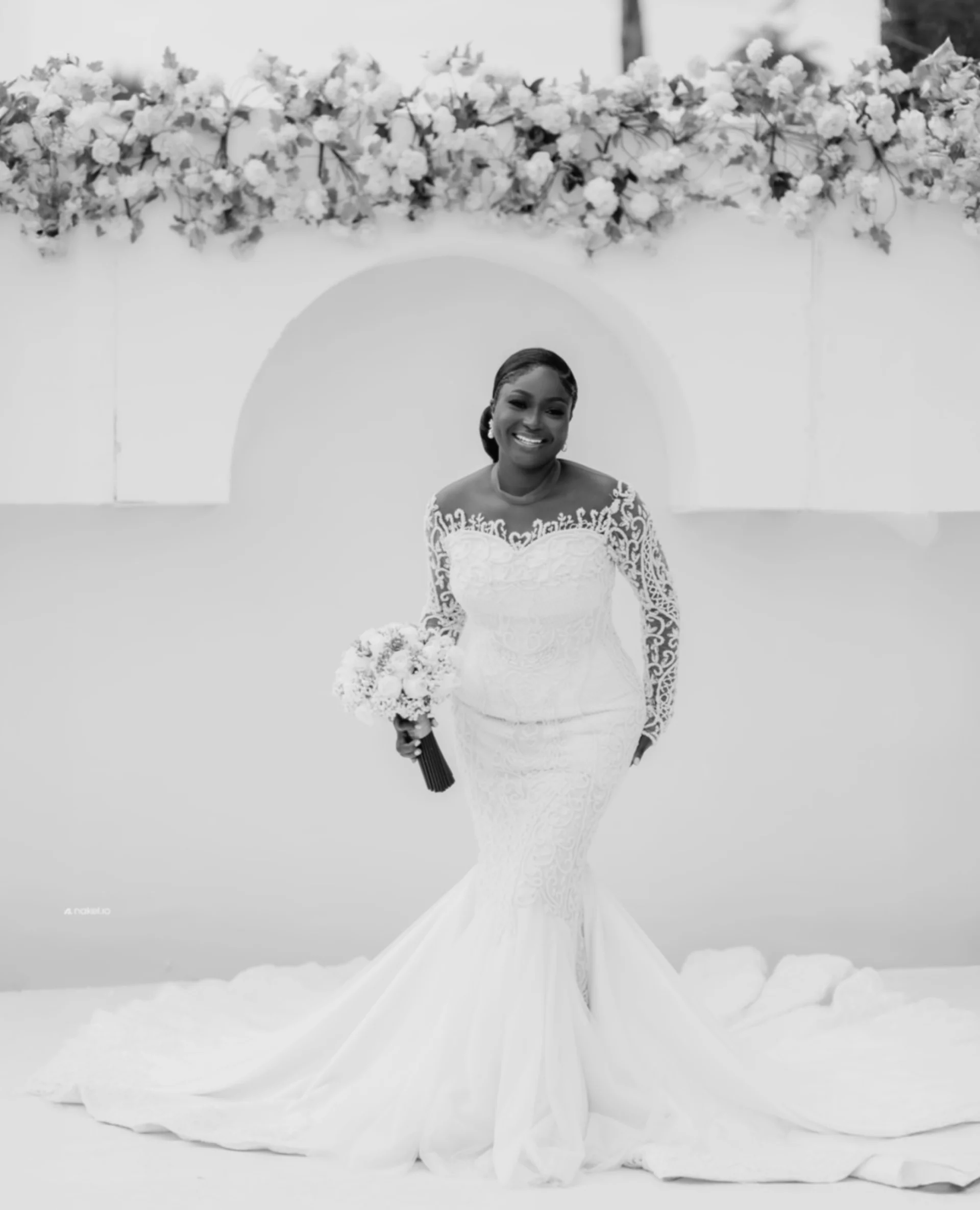 Bride smiling under a floral arch, black and white portrait